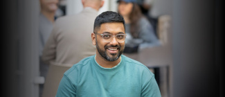 Male weekend MBA student smiling at the camera while a class is studying behind him