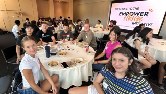 Photo of Michigan Ross Empower & Thrive Initiative students sitting at tables with white tablecloths. There is a screen in the background that has the Empower & Thrive maize and blue logo on it. 
