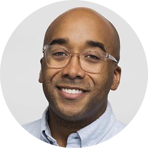 Professor Marcus Collins. A smiling person in a professional headshot wearing clear glasses and a light-colored shirt against a plain background.