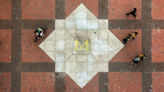 Image of the brass block M in the diag at the University of Michigan. There are four students walking around it but you can't see their faces. The photo is taken from up above. 