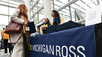 Two women talk at a registration table with a Michigan Ross banner.