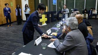 A presenter hands a paper to a panel of judges during a business and technology competition.