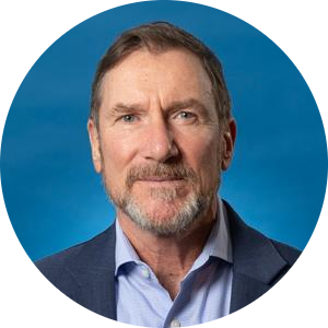 Professional headshot of a man wearing a blue blazer and light blue shirt against a blue background.