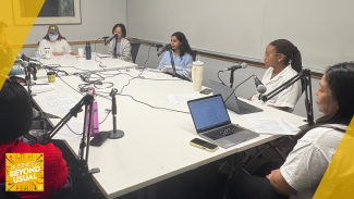 Six people sit around a table recording a podcast with microphones and laptops.
