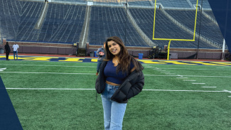 Person smiling and standing on a football field with stadium seats in the background.