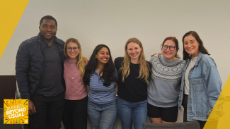 Six people smiling and standing together in a casual group indoors with the Business Beyond Usual Logo in the corner