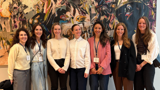 Photograph of seven women standing next to each other in front of a work of art