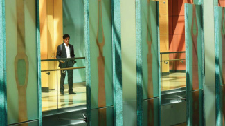 Person in business attire stands on a brightly lit balcony behind colorful architectural panels.