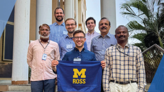 Seven people standing together outdoors, one holding a sign that reads "M ROSS".