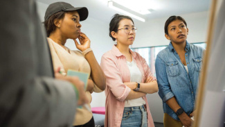 Three students attentively listen to a presentation in a classroom setting.