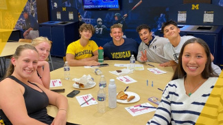 Group of people smiling around a table with plates of food at a Michigan-themed gathering.