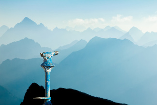 Public binoculars provide far view to distant blue mountain ranges silhouette in early Morning Sunlight.