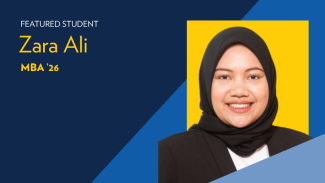 Text reads: Featured Student Zara Ali, MBA '26. A woman smiles, wearing black and white professional clothing in front of a blue and yellow background.