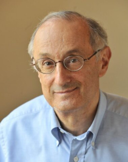 Portrait of an older man with glasses wearing a light blue collared shirt.