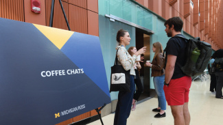 People gathered near a large blue "Coffee Chats" sign at a University of Michigan event.