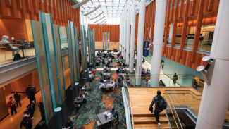Bustling multi-level atrium with people gathered at tables and seating areas under warm lighting.