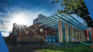 Modern glass-fronted building with sunlight streaming through, set against a blue sky.