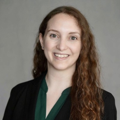 Francesca Colombo wearing a dark blazer and green blouse against a gray background.