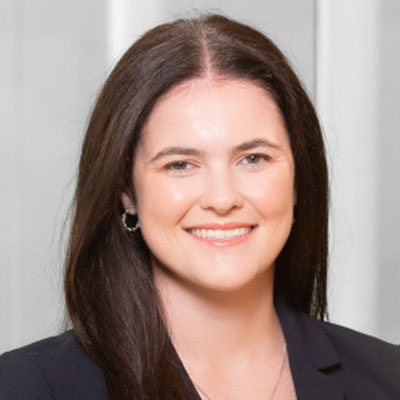 Headshot of Katie Corbett: A woman with long dark hair smiling and wearing a dark blazer.