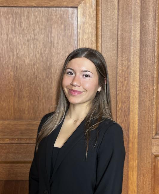 Maria Papp in a black blazer smiling in front of a wooden paneled wall.
