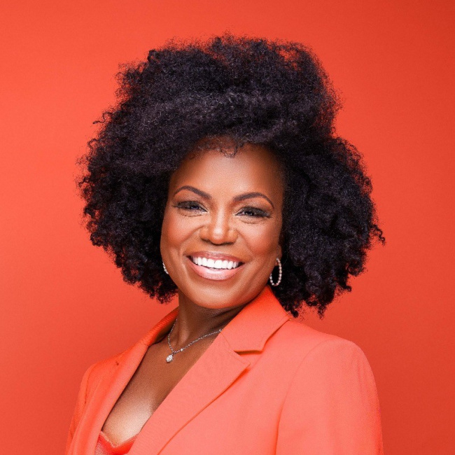 Smiling woman in an orange blazer against an orange background.