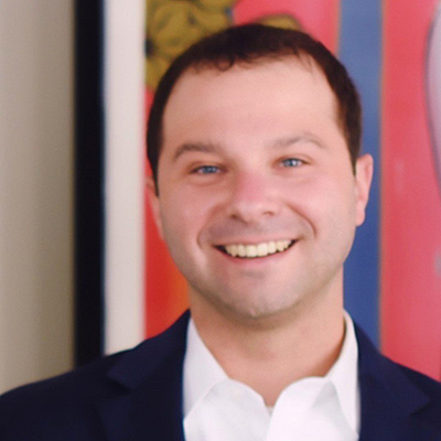 Smiling person in a suit standing in front of colorful artwork.