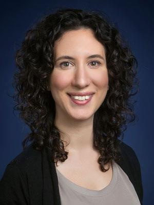 Professional headshot of a person with curly dark hair smiling at the camera.