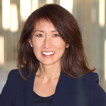 Smiling woman with shoulder-length dark hair wearing a navy blazer in a professional headshot.