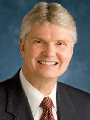 Professional headshot of Kim Cameron wearing a dark suit and red patterned tie.