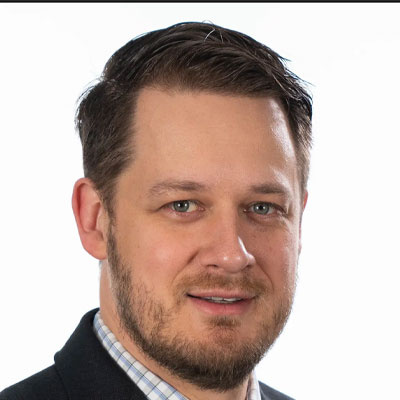 Professional headshot of Nick Sitarski with short brown hair and a beard, wearing a dark blazer.