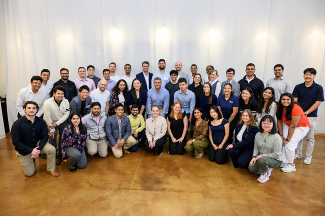 A large crowd of people stand in rows for a group photo in a bright room.