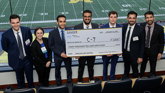 A group of seven individuals stands together, holding a large check for four thousand dollars, in a stadium setting.
