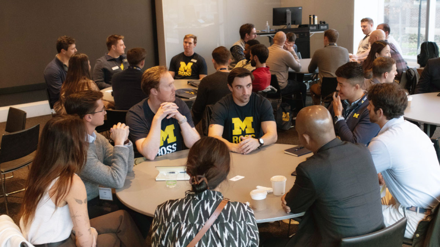 Group of students talking around a round table in a full room at Ross