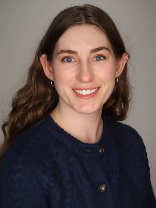 Person with long brown hair wearing a navy sweater, smiling at the camera against a neutral background.
