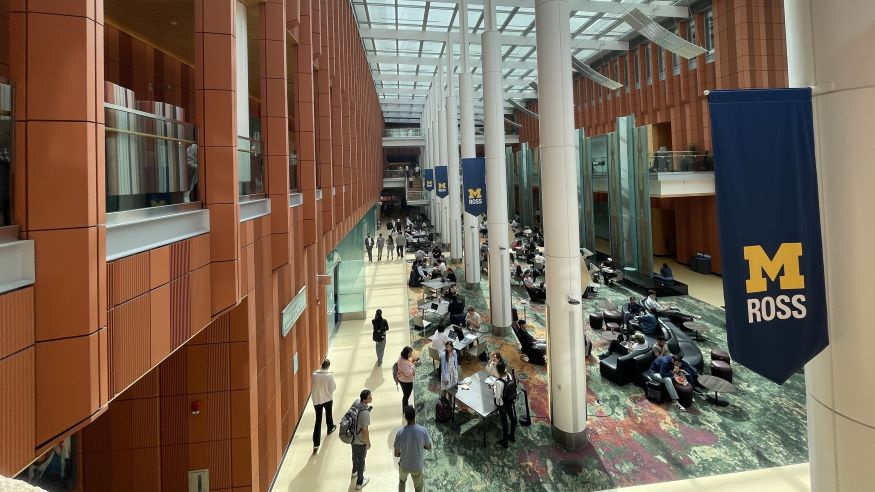 Photo of the Michigan Ross Winter Garden. The photo is taken from up above and is looking down into the space. There are a number of students sitting at tables who are studying and working together. 