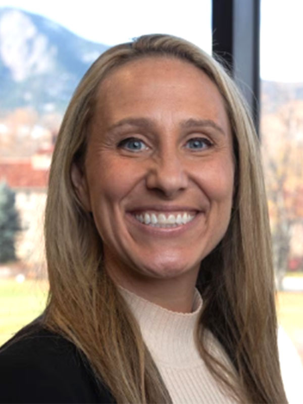 Aimee Mandolini in business attire, mountains visible through window behind her.