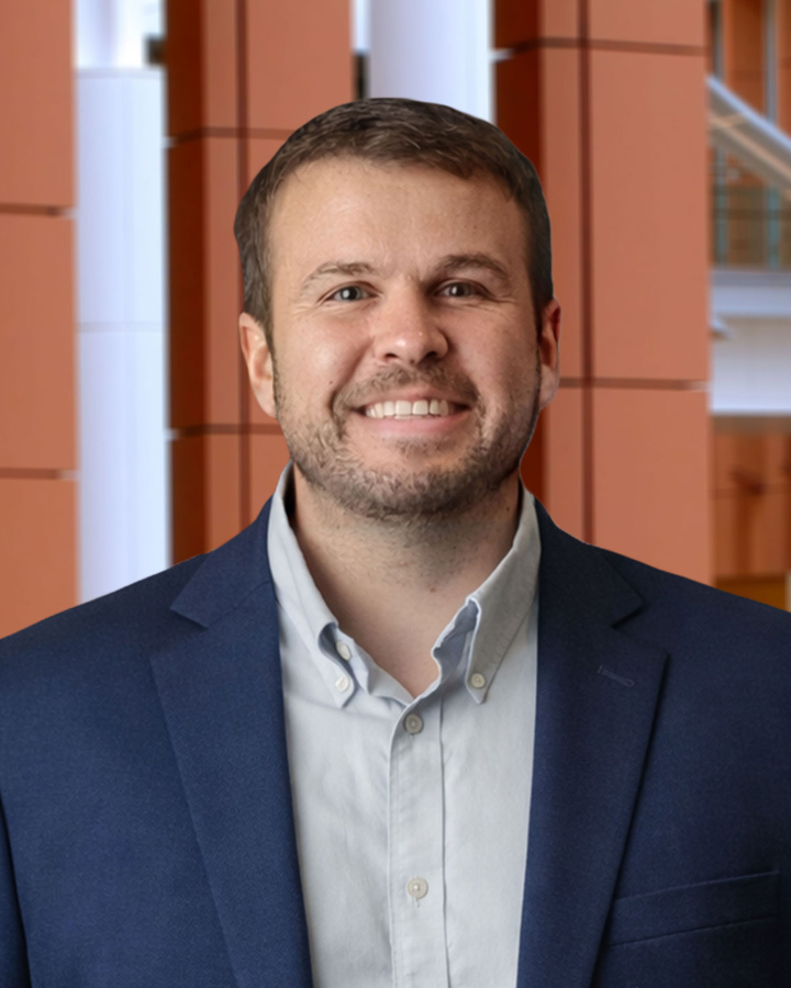 Cory Phinney a blue blazer smiling in an indoor atrium with orange columns.