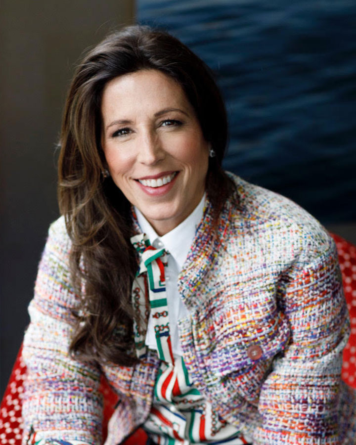 Jenny Just wearing a colorful blazer and patterned blouse, smiling at the camera.