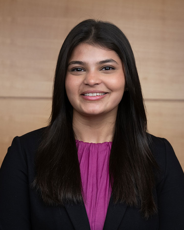 Jiya Sheth in professional attire against a plain wooden background.