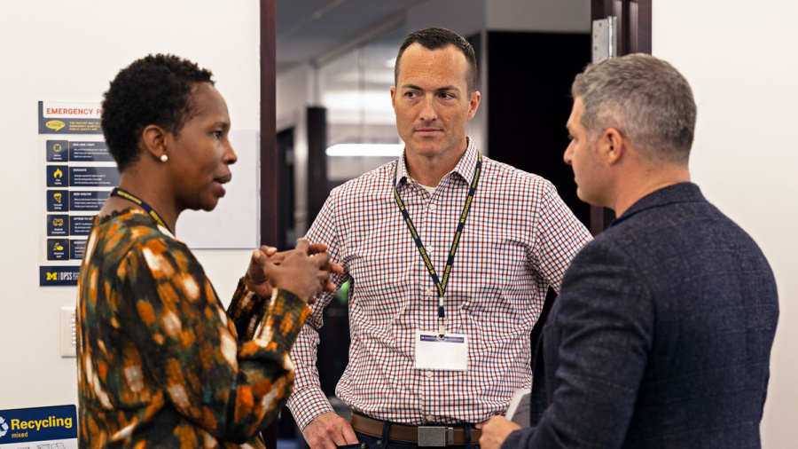 Three people have a serious conversation in an office hallway.