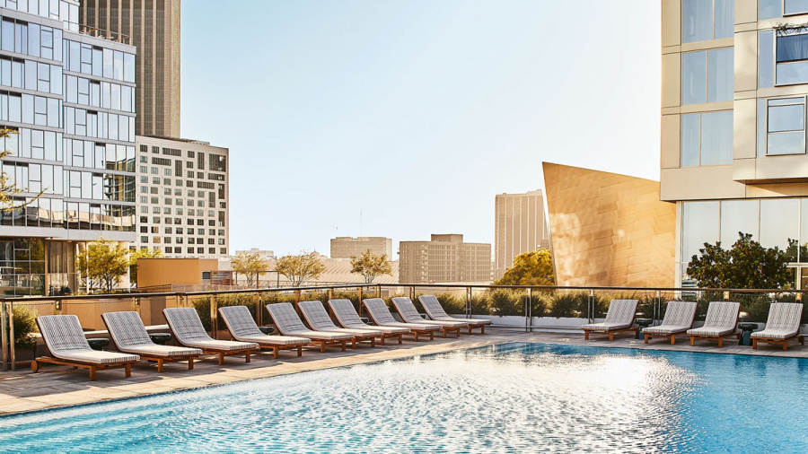Modern outdoor pool area with lounge chairs, surrounded by city buildings on a sunny day.