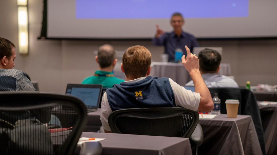 Person in a classroom raises hand to ask a question during a lecture.