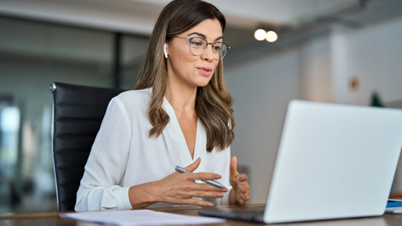 Person wearing glasses having a video call and speaking at a laptop in an office.