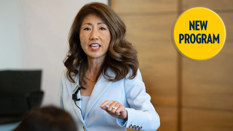 Woman in light blazer gestures while speaking, with a yellow "New Program" badge in the corner.