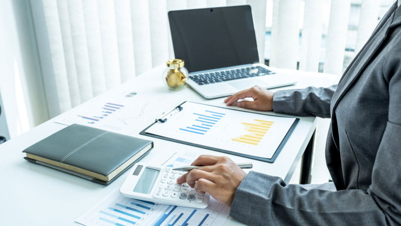 Person analyzing financial charts and using a calculator at an office desk.