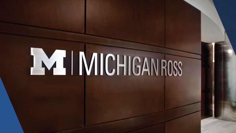 The Michigan Ross logo displayed in silver on the dark wood wall of the school building.