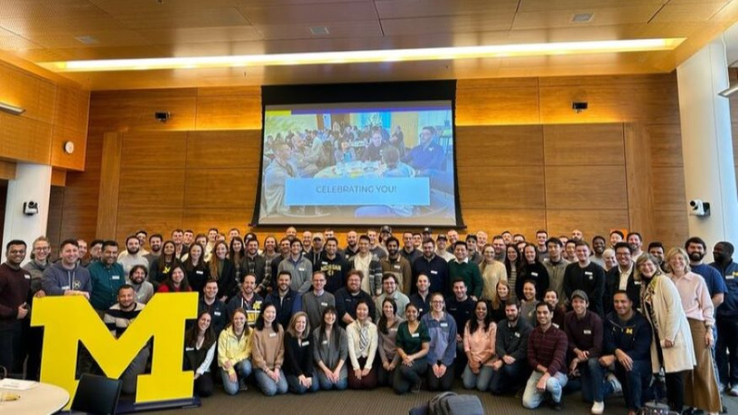 Large group of students standing together behind a large yellow block M. 