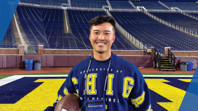 A man in a Michigan sweatshirt poses on the field in the Big House