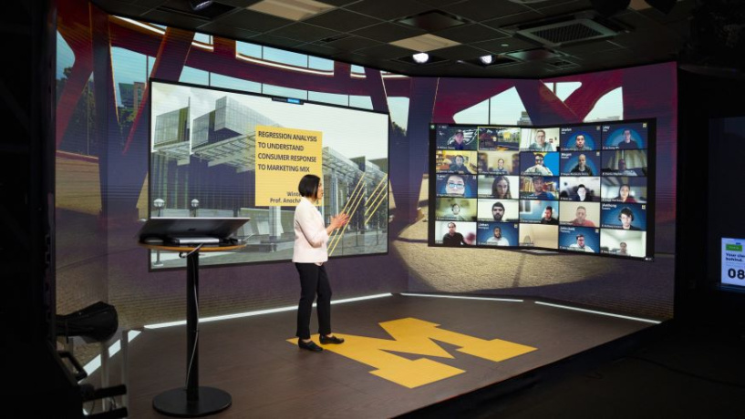 Photo of the Online MBA studio with a Michigan Ross professor standing in the middle of the studio looking at a number of students on screen. 
