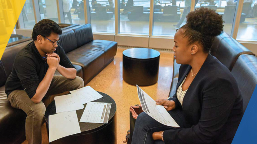 Two people sitting in an office discussing documents spread out on a table.